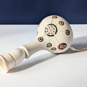 May include: White ceramic table lamp with a round base decorated with brown and green circles. The lamp has a white cord.