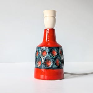 Op de afbeelding: Een rode en blauwe keramische tafellamp met een witte keramische lampenkap. De lamp heeft een bloemenpatroon met blauwe en groene swirls.