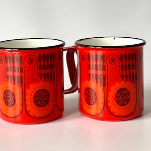 May include: Two red enamel mugs with a black rim and a brown and orange geometric pattern. The mugs have a white interior.