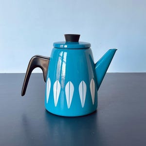 May include: A teal enamelware teapot with a black handle, lid, and spout. The teapot features a white feather design on the body. The teapot is a vintage style and is suitable for brewing tea or coffee.