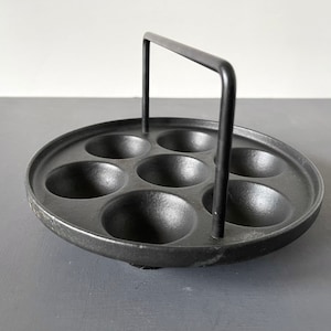 May include: Black cast iron egg poacher with six individual molds and a black metal handle.