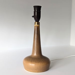 May include: A brown ceramic table lamp with a black lampshade and a gold accent. The lamp has a rounded base and a tall, slender neck.