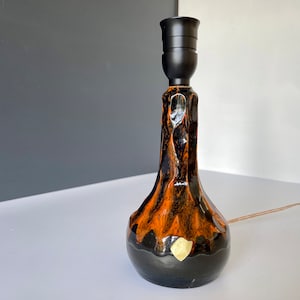 May include: A black and orange ceramic table lamp with a black lampshade. The lamp has a gold accent on the bottom.