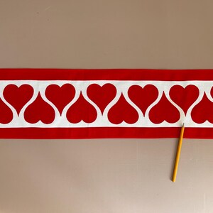 May include: Red fabric trim with a white heart pattern. The trim has a white background with red hearts that are outlined in white.