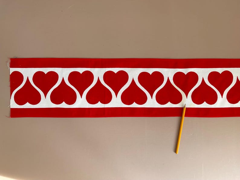May include: Red fabric trim with a white heart pattern. The trim has a white background with red hearts that are outlined in white.