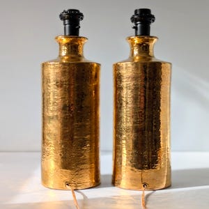 May include: A pair of gold ceramic table lamps with black lampshades. The lamps have a hammered texture.