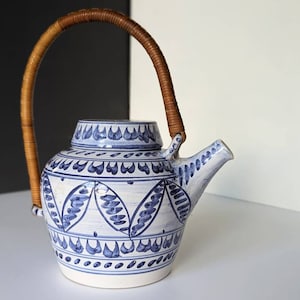 May include: A white ceramic teapot with a blue and white floral design and a brown wicker handle.