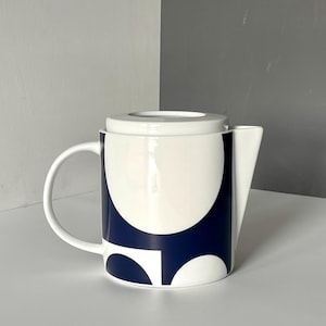 Pode incluir: Bule de cerâmica branco com um padrão geométrico azul marinho e branco. O bule tem uma alça curva, um bico e uma tampa a condizer. O design apresenta formas grandes e arredondadas. Um acessório de chá moderno.