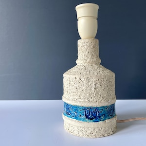 May include: A white ceramic table lamp with a blue and white patterned band around the base. The lamp has a white ceramic shade.