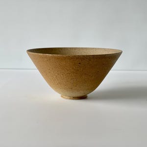 May include: A small, brown ceramic bowl with a speckled glaze. The bowl is slightly wider at the top than the bottom and has a rounded base.