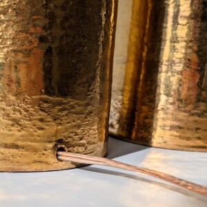 May include: Two gold-toned table lamps with a textured finish and a cord connecting them.