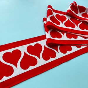 May include: Red and white fabric trim with a repeating pattern of white hearts on a red background.