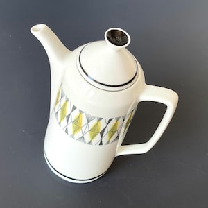 Puede incluir: Cafetera de cerámica blanca con tapa negra y un patrón geométrico en negro, amarillo y verde.