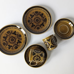 Puede incluir: Un juego de tazas y platillos de té de cerámica con estampado marrón y negro. Las tazas y los platillos presentan un diseño geométrico con un motivo floral.