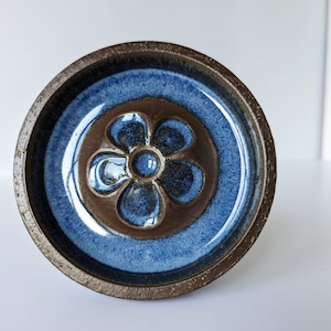 Peut inclure: Un plat en céramique bleu et brun avec un motif de fleur en relief au centre.