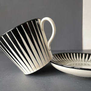 May include: A black and white striped ceramic teacup and saucer set. The cup has a white interior and a black handle. The saucer has a black rim and a white center.