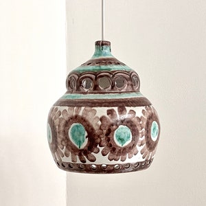 May include: A ceramic pendant light with a white, brown, and green floral pattern. The light has a round shape and a decorative, openwork top.