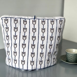 Puede incluir: Cubierta de cesta de pan de lino blanco con un patrón geométrico azul y gris de flechas.