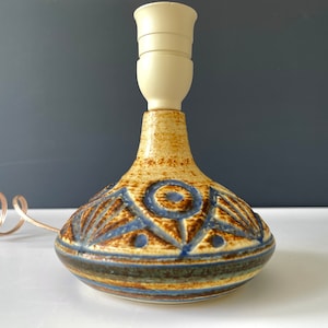May include: A ceramic table lamp with a brown, blue and white geometric design. The lamp has a white ceramic shade and a coiled cord.