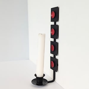Puede incluir: Candelero de pared de metal negro con una vela blanca y cuatro círculos rojos.