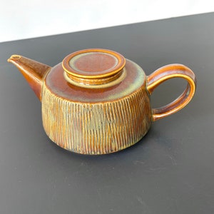 May include: A brown ceramic teapot with a textured, ribbed design. The teapot has a lid and a handle.