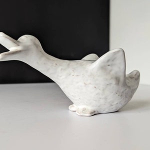 May include: White ceramic duck figurine with a speckled glaze. The duck has its head tilted back and its beak open.