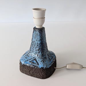 May include: A blue and brown ceramic table lamp with a white ceramic lampshade. The lamp has a geometric pattern and a cord with a switch.