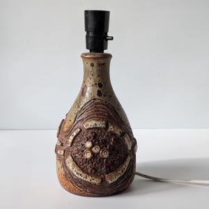 May include: A brown and white ceramic table lamp with a geometric design. The lamp has a black lampshade and a cord.