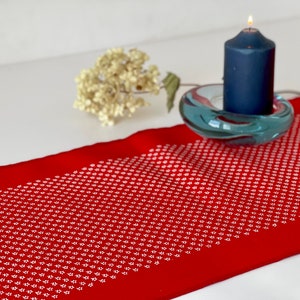 Könnte beinhalten: Ein roter Tischläufer mit einem weißen Muster aus kleinen Punkten. Eine blaue Kerze steht in einem gläsernen Kerzenhalter auf dem Läufer.