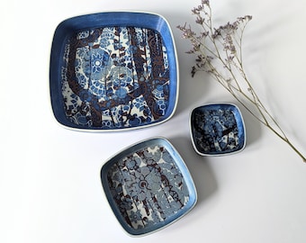 May include: Three square ceramic dishes with a blue and white floral pattern. The dishes are nested inside each other, with the largest dish on the bottom and the smallest dish on top.