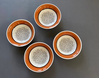 以下が含まれることがあります： グレーの背景に、茶色の縁取りとグレーの花柄が描かれた白いセラミックボウルが4つあります。ボウルは円形に配置されています。
