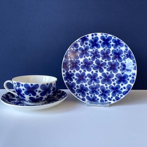 May include: A blue and white floral teacup and saucer set. The cup and saucer feature a repeating pattern of blue flowers on a white background.