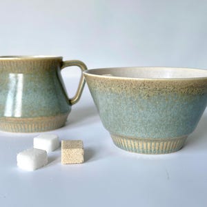 May include: A green and brown ceramic creamer and sugar bowl set. The creamer has a handle and a textured surface. The sugar bowl is round and has a textured surface.