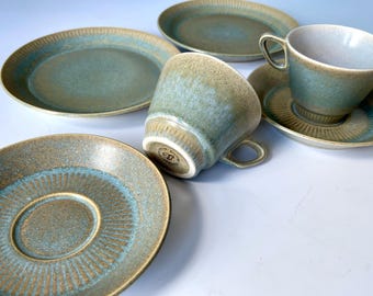 Może przedstawiać: Zestaw czterech zielonych i brązowych ceramicznych filiżanek do herbaty i spodków. Filiżanki mają fakturowaną, kropkowaną glazurę, a spodków mają koncentryczny wzór koła.