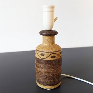 May include: A brown and tan ceramic table lamp with a white lampshade. The lamp has a geometric design.