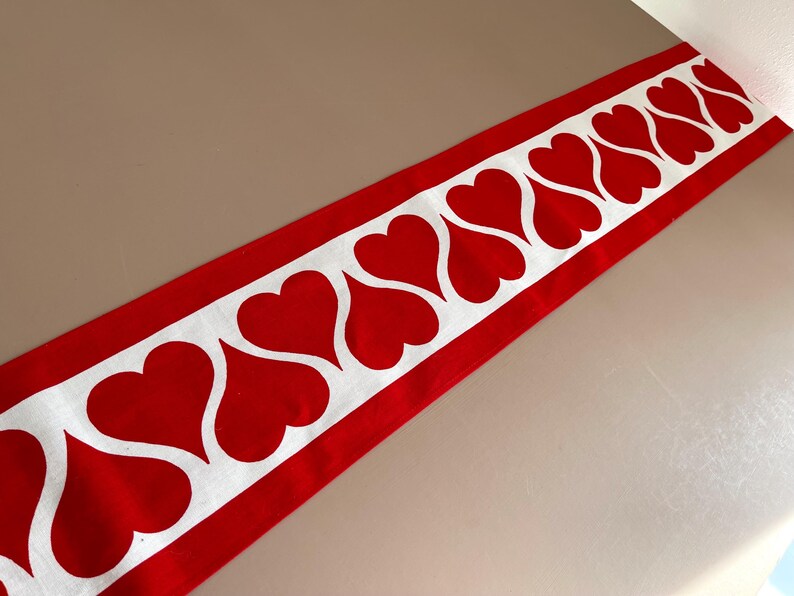 May include: Red and white table runner with a repeating pattern of white hearts on a red background.