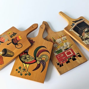 Könnte beinhalten: Vier Schneidebretter aus Holz mit verschiedenen Designs. Eines zeigt einen Hahn, ein anderes einen Koch beim Kochen, eines ein Weinglas und eine Kerze und das letzte einen Kamin.