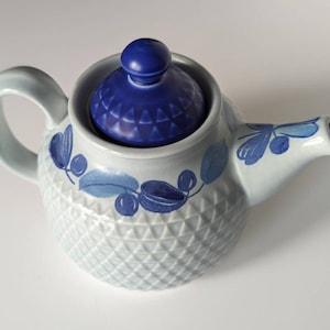 以下が含まれることがあります： 青い蓋と花柄の青い白のセラミックティーポット。ティーポットはテクスチャ加工された表面と丸いボディを持っています。