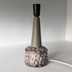 May include: A ceramic table lamp with a textured, gray base and a black lampshade. The base has a textured, bumpy surface.