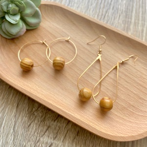 May include: A set of gold hoop earrings and gold teardrop earrings with wooden beads. The beads are a light brown color with a wood grain pattern.