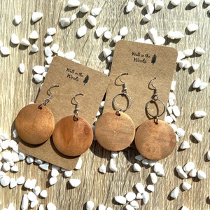 May include: Two pairs of wooden earrings with silver hooks. The earrings are round and have a natural wood finish. The earrings are displayed on brown card stock with the text "Walk in the Woods" printed on them.