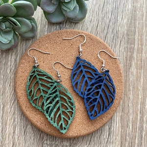 May include: A pair of leaf-shaped earrings, one green and one blue. The earrings are made of wood and have a delicate, intricate design.