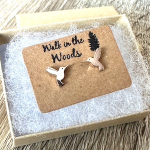 May include: A pair of silver hummingbird earrings in a small brown box with a white paper insert. The insert has the text "Walk in the Woods" and a small pine tree graphic.