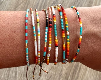 May include: A set of colorful beaded bracelets with a variety of patterns and colors, including red, orange, yellow, green, blue, and white. The bracelets are tied with brown cords.