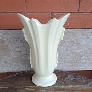 Peut inclure: Un vase en céramique blanc avec un motif cannelé et des poignées décoratives. Le vase a un style classique et élégant.