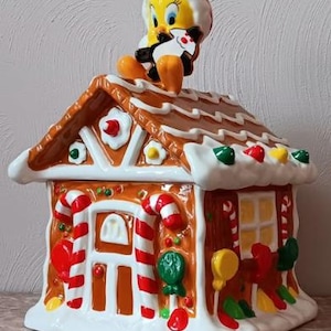 Pode incluir: Um pote de biscoitos de cerâmica em forma de casa de gengibre com uma figura do personagem de desenho animado Piu-Piu no topo. A casa é decorada com bengalas doces, gomas e glacê.