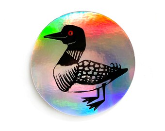 May include: A black and white illustration of a loon with a red eye on a holographic sticker with rainbow colors.