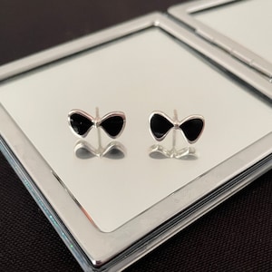 Puede incluir: Un par de pendientes de plata en forma de lazo con esmalte negro.