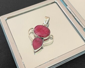 May include: A silver pendant featuring two red ruby stones. The larger stone is oval shaped and the smaller stone is teardrop shaped.