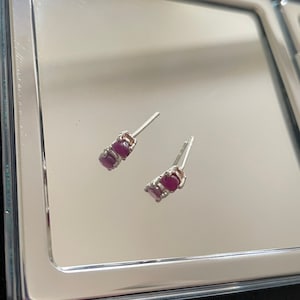 May include: A pair of silver stud earrings with two small, round, pink gemstones.